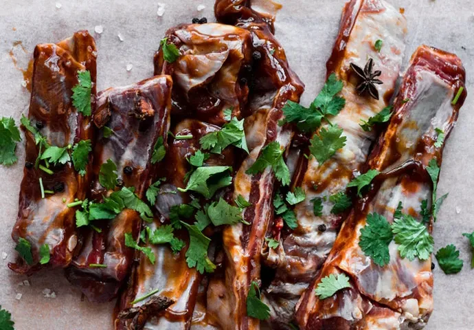 Lamb ribs with sauce and chopped herbs on parchment