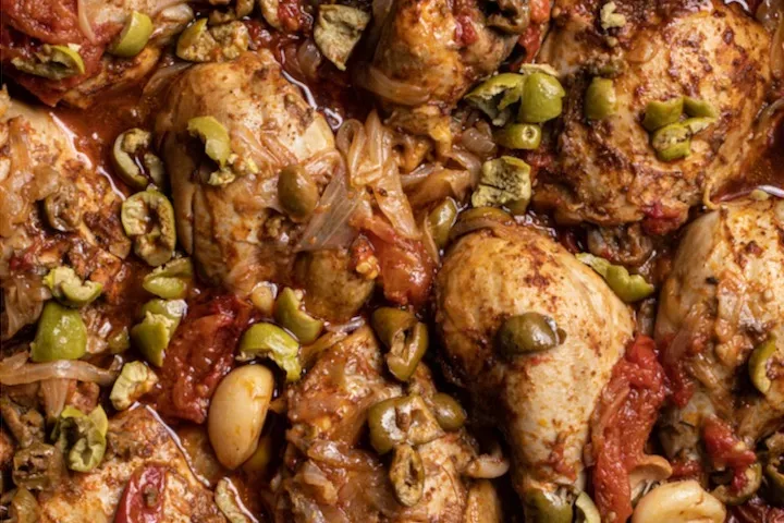 Close up shot of chicken pieces in red sauce with chopped green olives.